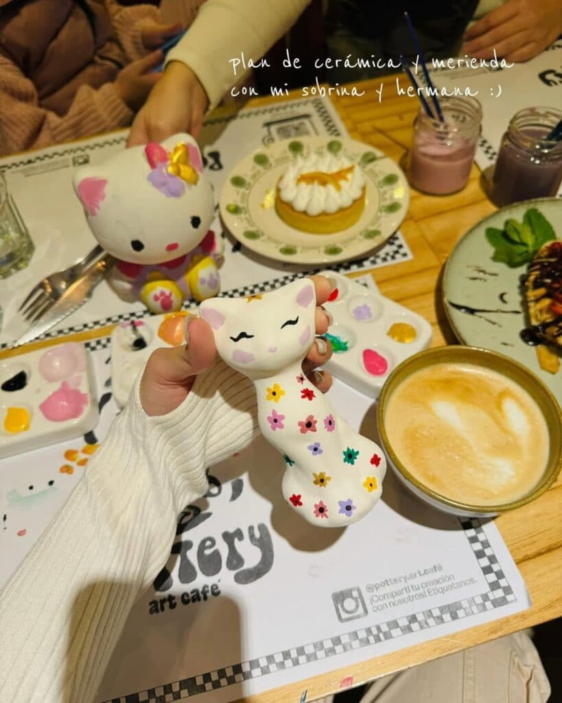 Mano sosteniendo un gato de cerámica pintado a mano, mesa con paletas, Hello Kitty, café y merienda en Pottery Art Café — imagen 2 de 4