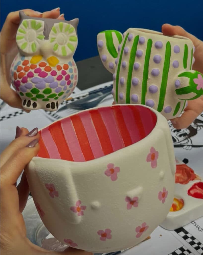 Tres manos muestran piezas terminadas: búho multicolor, taza en forma de cactus y cuenco con rayas rojas y rosas — imagen 4 de 4